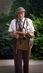 Dr. Jazz wearing a world War One-era army helmet and carrying a washboard festooned with a bicycle horn, cowbell and other noise-making items